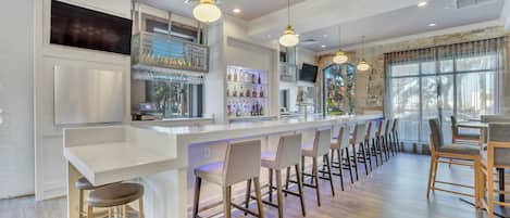 Un área de bar moderna con una barra larga, varios taburetes e iluminación colgante.