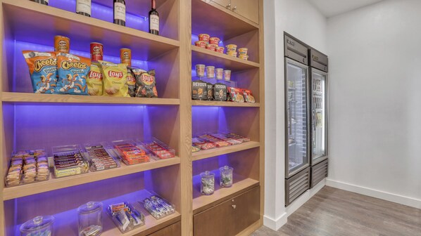 Un área de almacenamiento con estantes que contienen aperitivos, bebidas y un refrigerador.