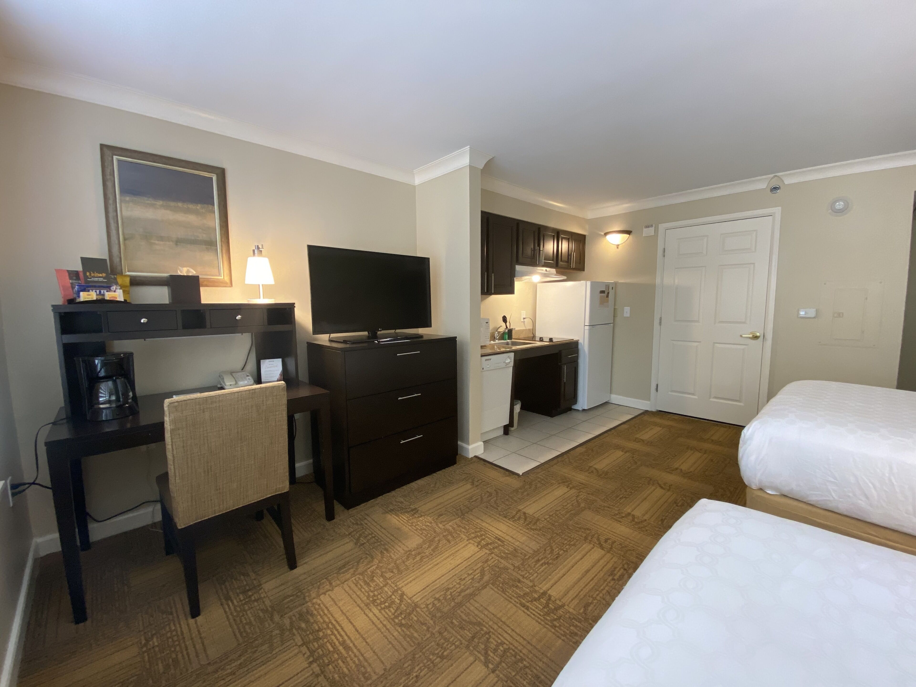 A hotel room with a desk, chair, television, kitchenette, and two beds.
