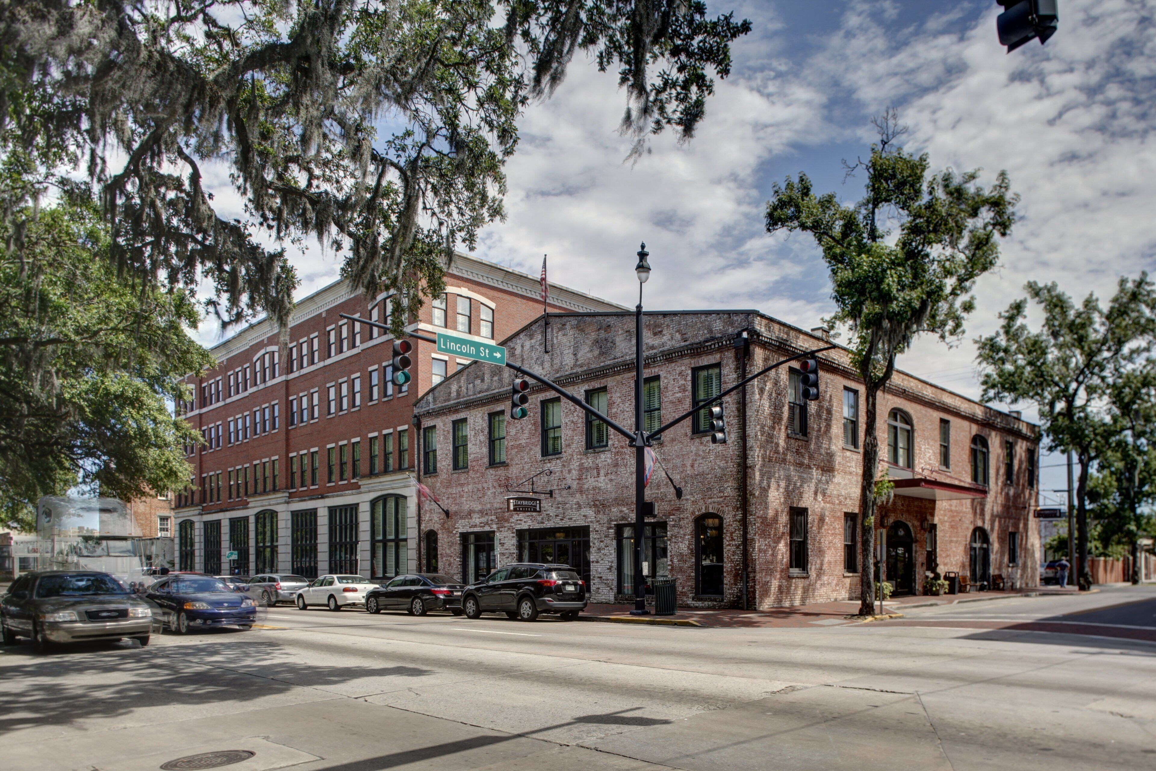 A street corner with a brick building, a traffic light, and cars on the road.