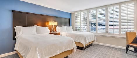 Une chambre d’hôtel avec deux lits, une table de chevet avec une lampe, une fenêtre avec des stores et une chaise.