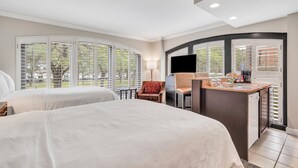 A hotel room with two beds, a desk with a flat-screen TV, a chair, and a view of the outdoors through large windows. - Staybridge Suites Savannah Historic District by IHG (Savannah)