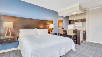 Quarto de hotel com uma cama grande, duas mesinhas de cabeceira com abajures, uma kitchenette pequena e uma parede azul de destaque.