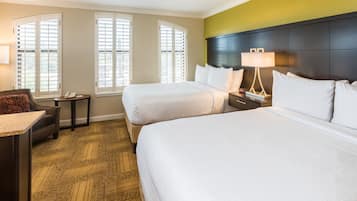 A hotel room with two beds, a desk, a chair, a nightstand, and a lamp.