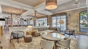 Un moderno vestíbulo de hotel con zona de bar, áreas de descanso y amplios ventanales que permiten la entrada de luz natural.