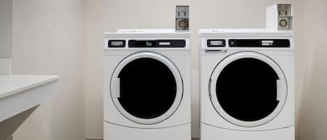 Two white front-loading washing machines in a laundry room with a white sink and a tiled floor.