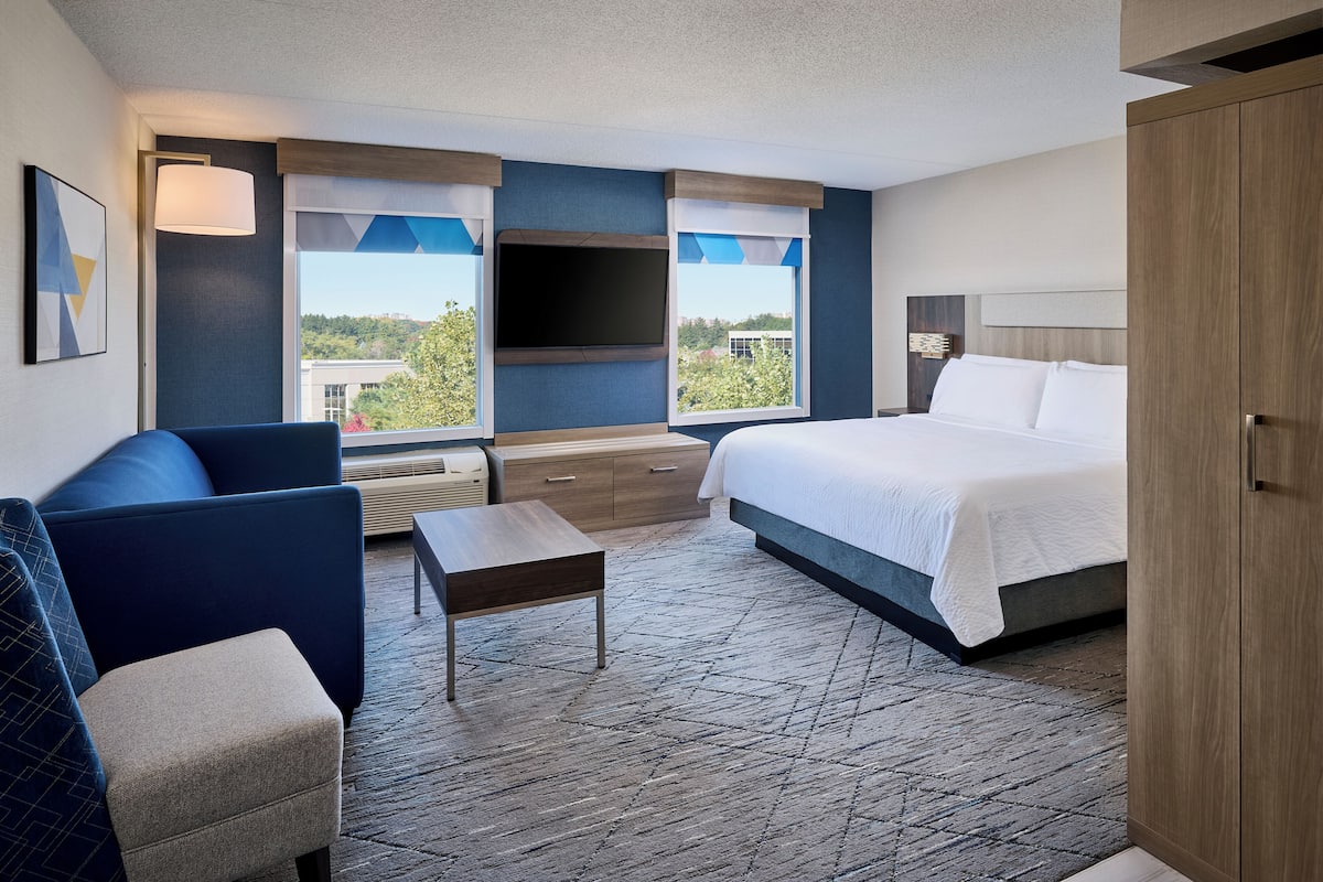 A modern hotel room with a large bed, a sofa, a small table, and a TV.