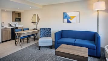 Ein modernes Hotelzimmer mit Essbereich, einem blauen Sofa, einem kleinen Tisch und einer Lampe.