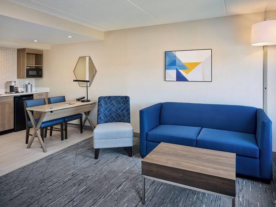 Ein modernes Hotelzimmer mit Essbereich, einem blauen Sofa, einem kleinen Tisch und einer Lampe.