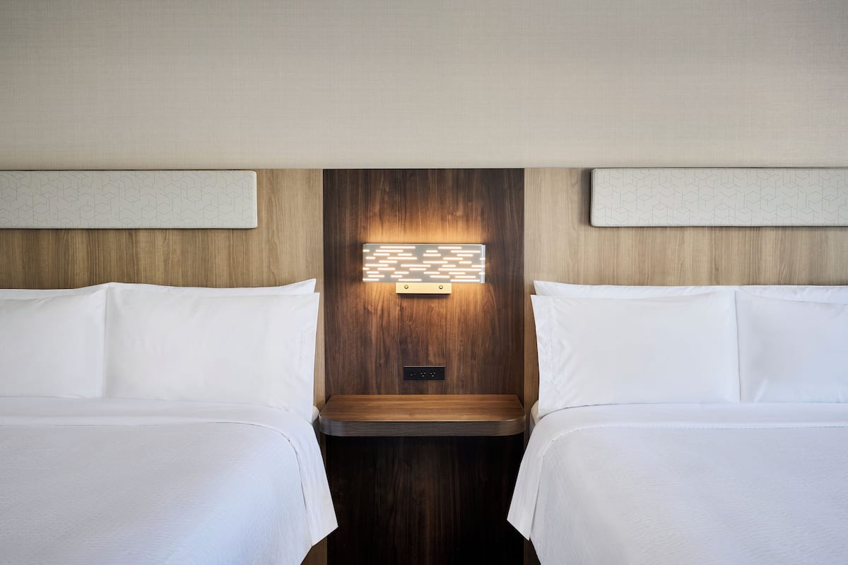 A hotel room with two beds, a wooden headboard, and a wall-mounted light fixture.