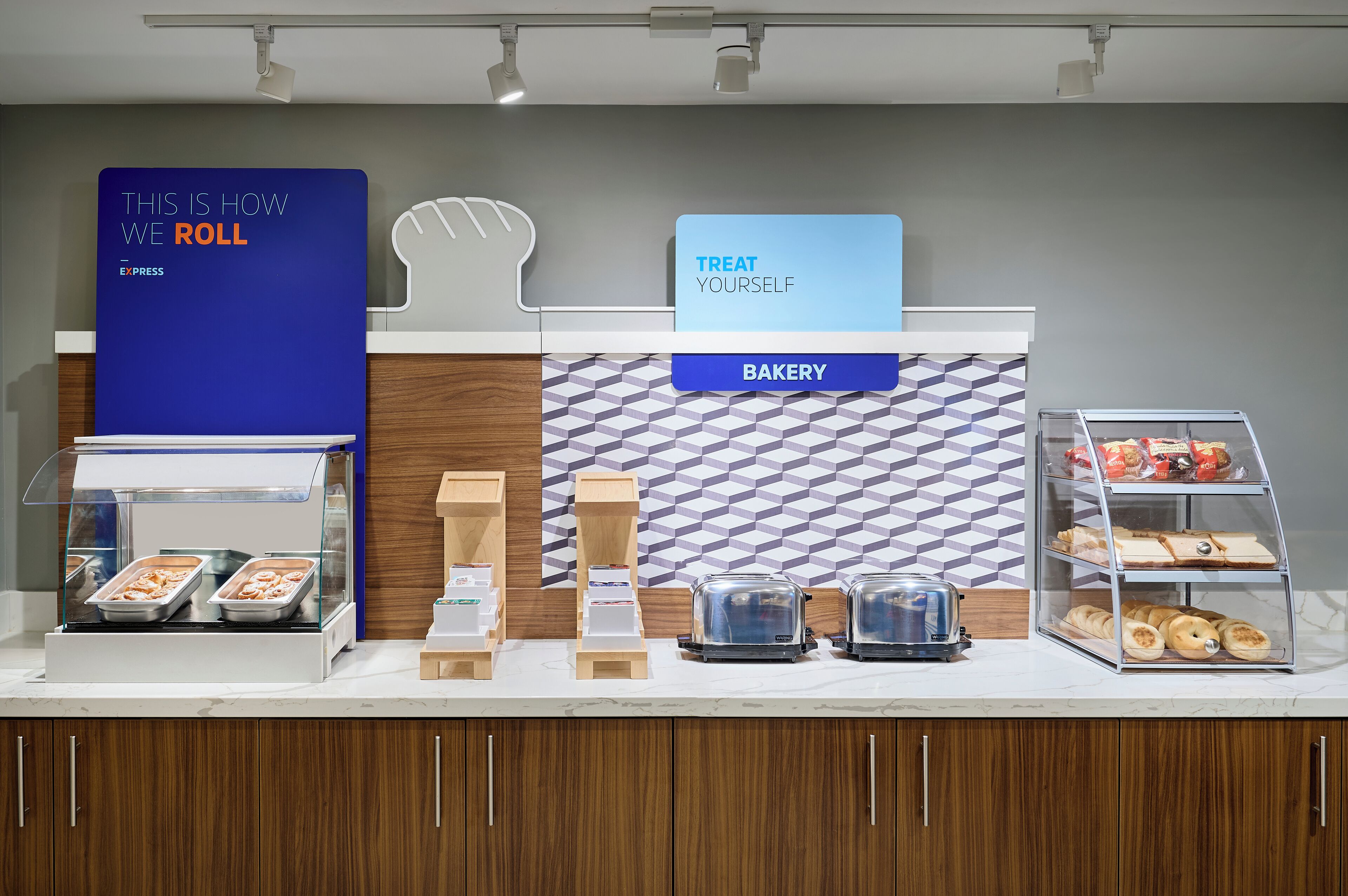 A bakery counter with trays of pastries, a coffee machine, and a sign that says "TREAT YOURSELF".