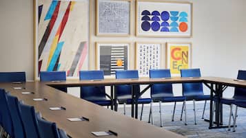 Un salón de conferencias con una larga mesa, sillas azules y obras de arte enmarcadas en la pared.