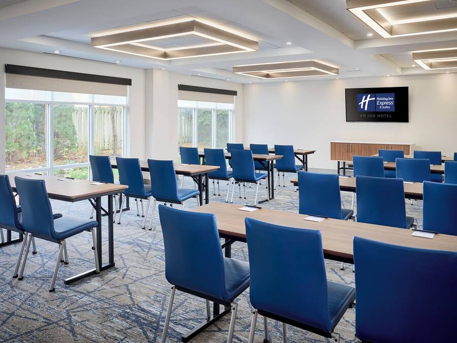 A conference room with blue chairs and tables, large windows, and a flat-screen TV on the wall.
