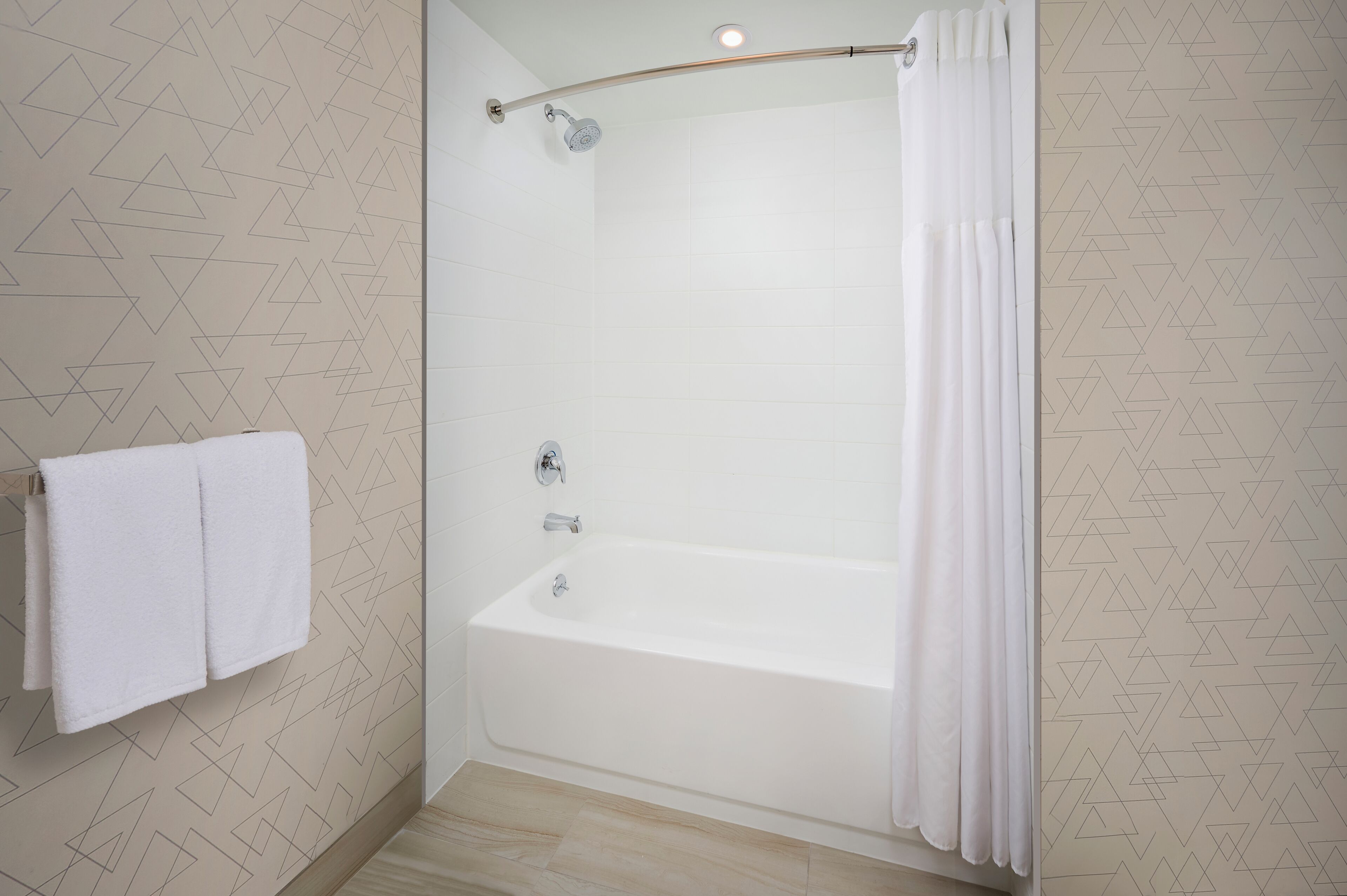 A modern bathroom with a glass-enclosed shower, white tiled walls, and a geometric pattern.
