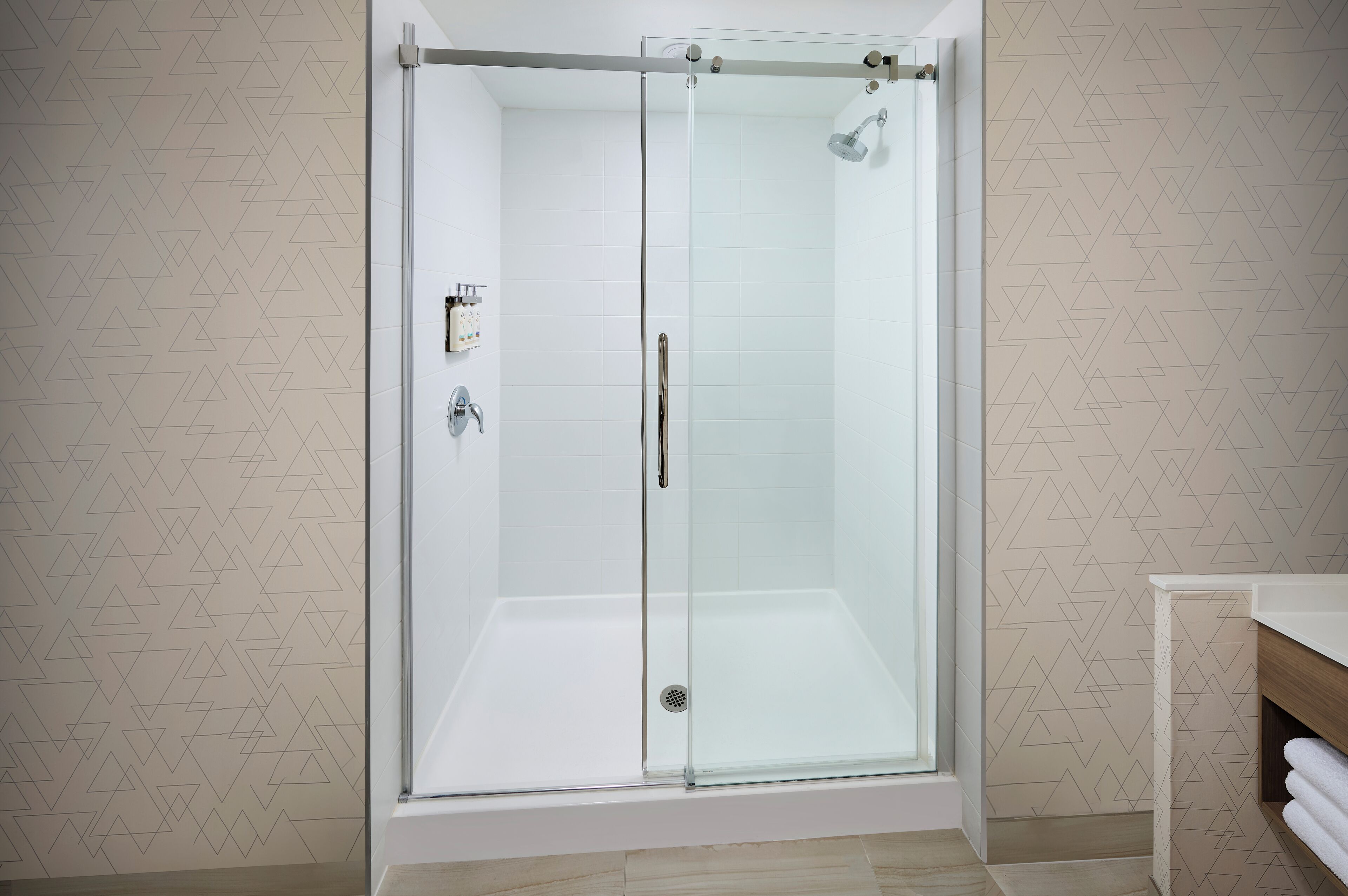 Una cabina doccia in vetro con parete rivestita in piastrelle bianche e una panca in legno.