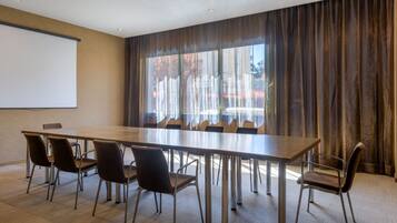 A conference room with a long table, six chairs, a projector screen, and large windows with curtains.