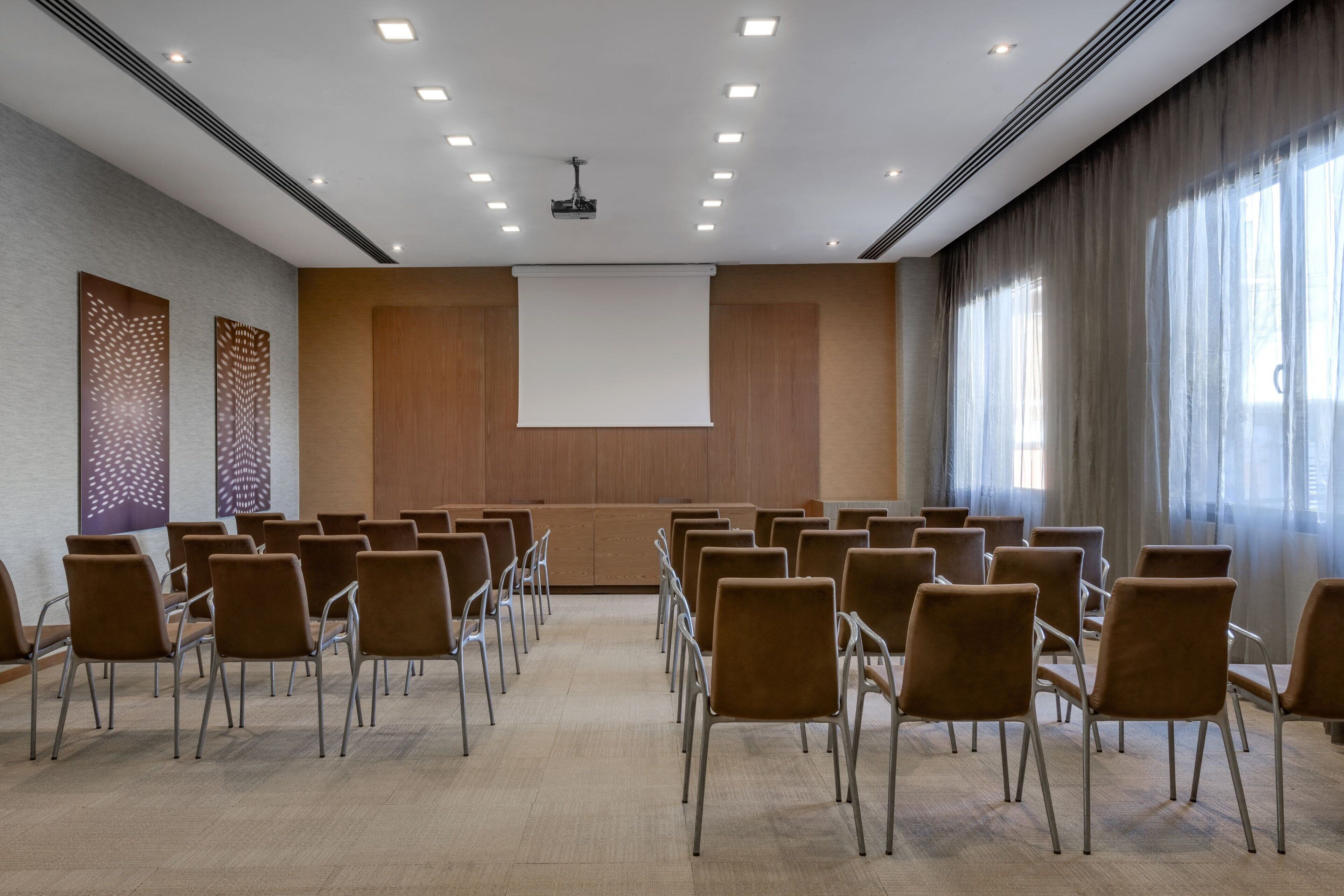 A conference room with rows of chairs, a projector screen, and a large window with curtains.