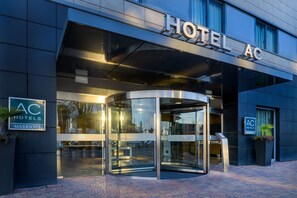 A modern hotel entrance with a revolving door, glass facade, and signage for "HOTEL AC" and "AC HOTELS MARRIOTT".