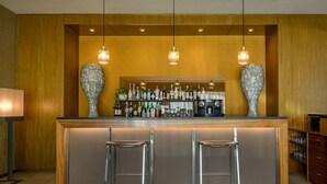 Un coin bar avec un fond en bois, deux tabourets et une variété de bouteilles d’alcool.