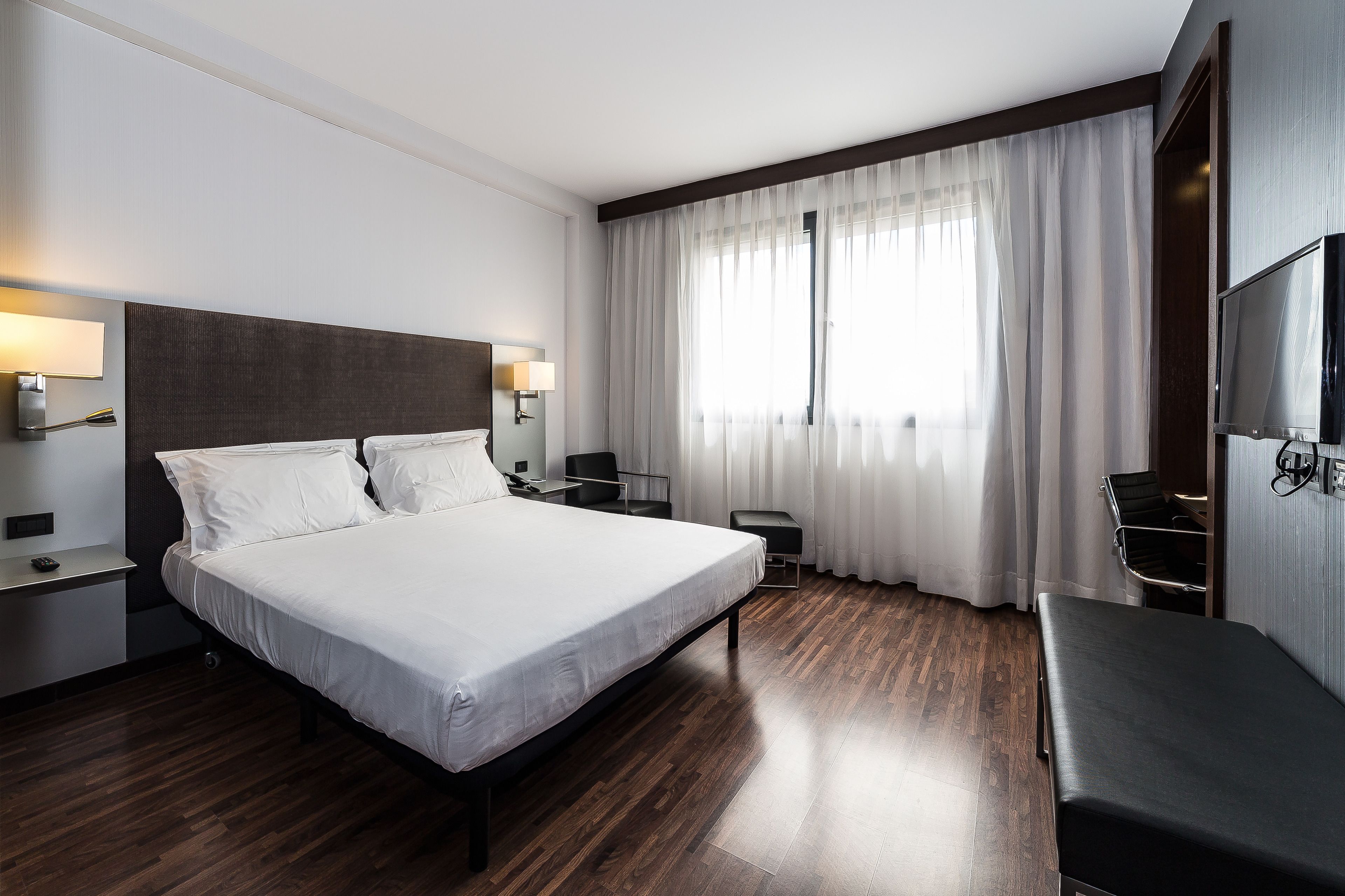 Une chambre d’hôtel moderne avec un grand lit, des tables de chevet, une télévision et un banc.
