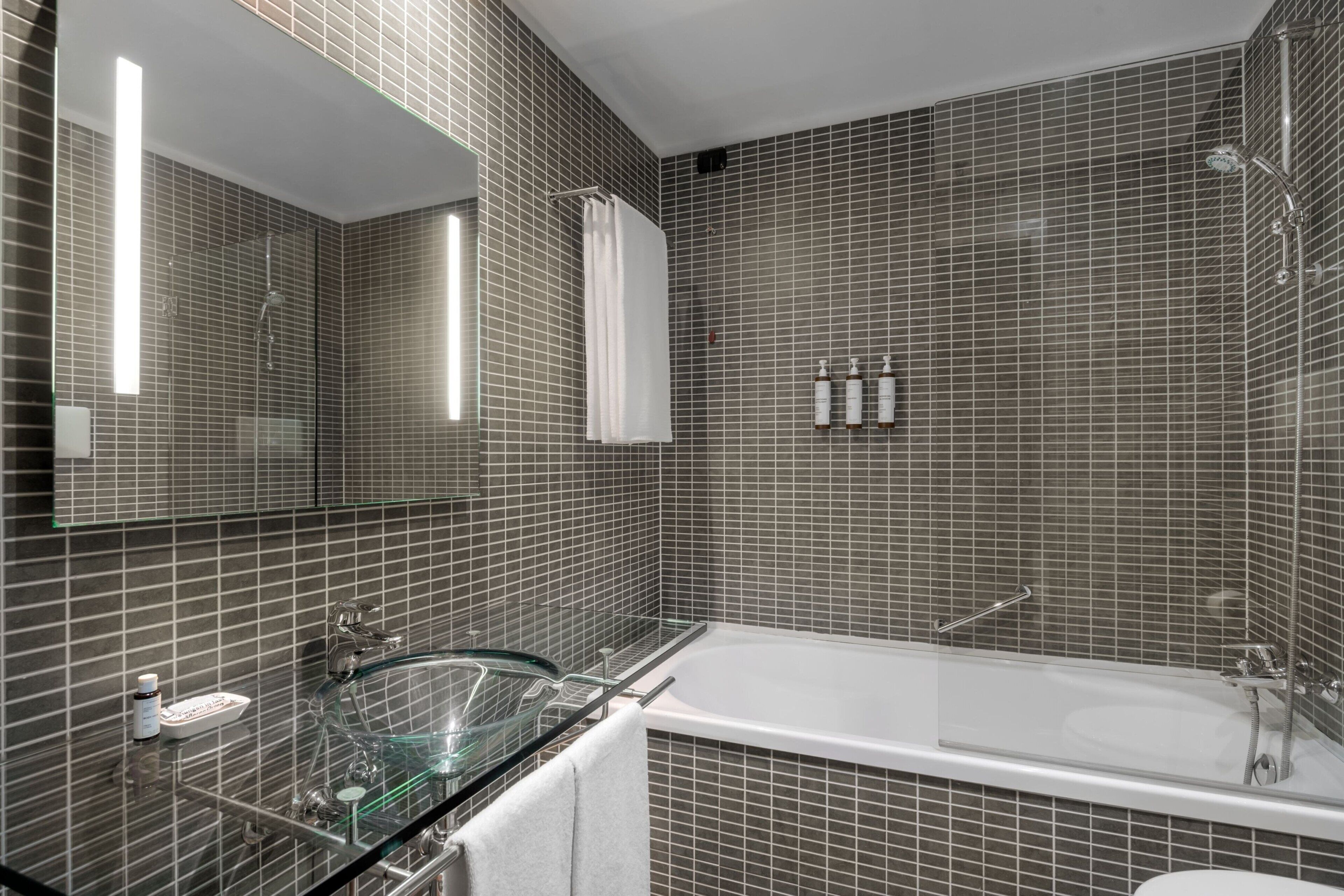 A modern bathroom with a glass-enclosed sink, a large bathtub, and a tiled shower area.