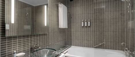 Un baño moderno con lavamanos de vidrio, una bañera grande y una zona de ducha con azulejos.