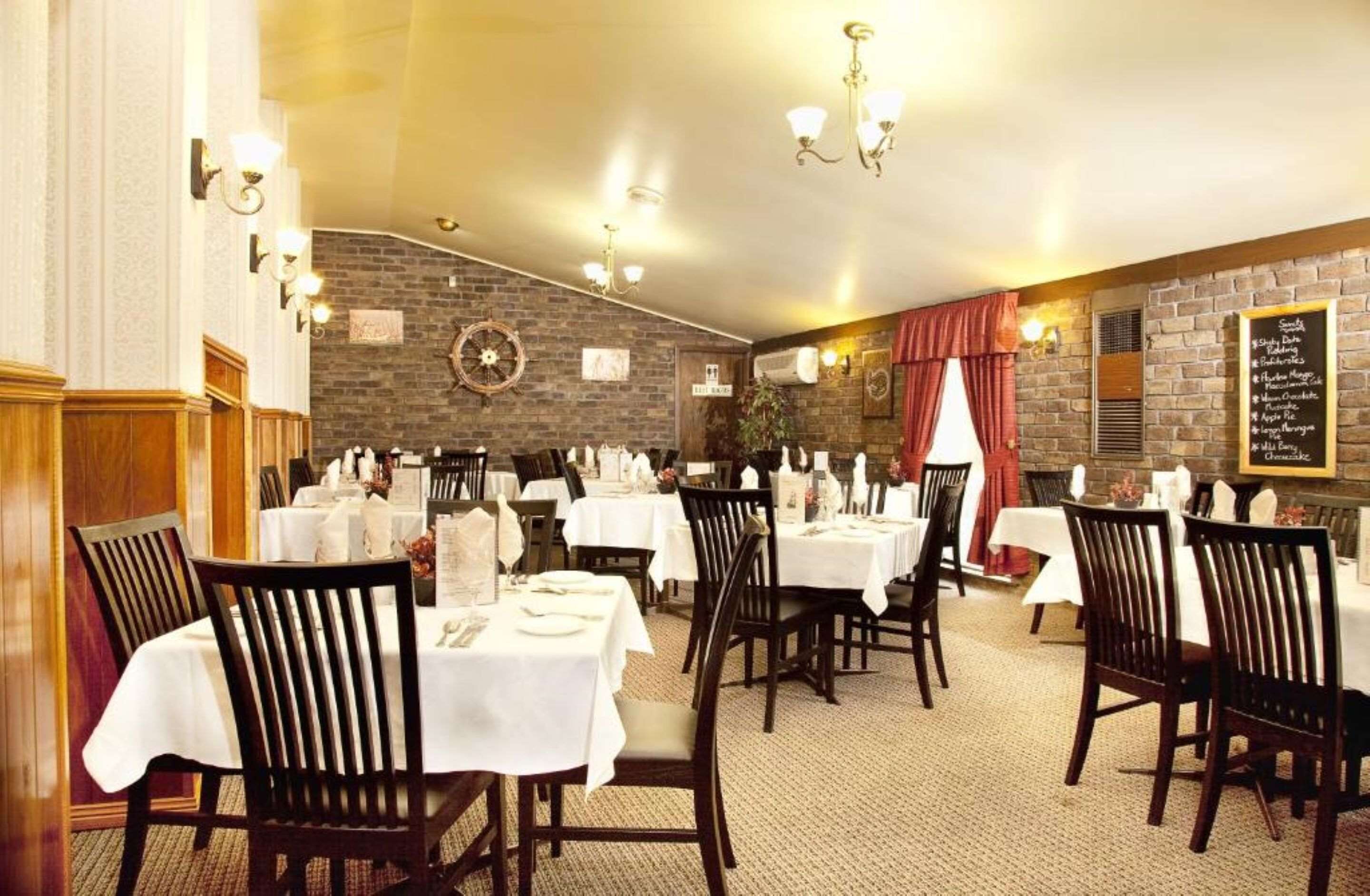 A restaurant with multiple tables and chairs, a brick wall, and a menu board.