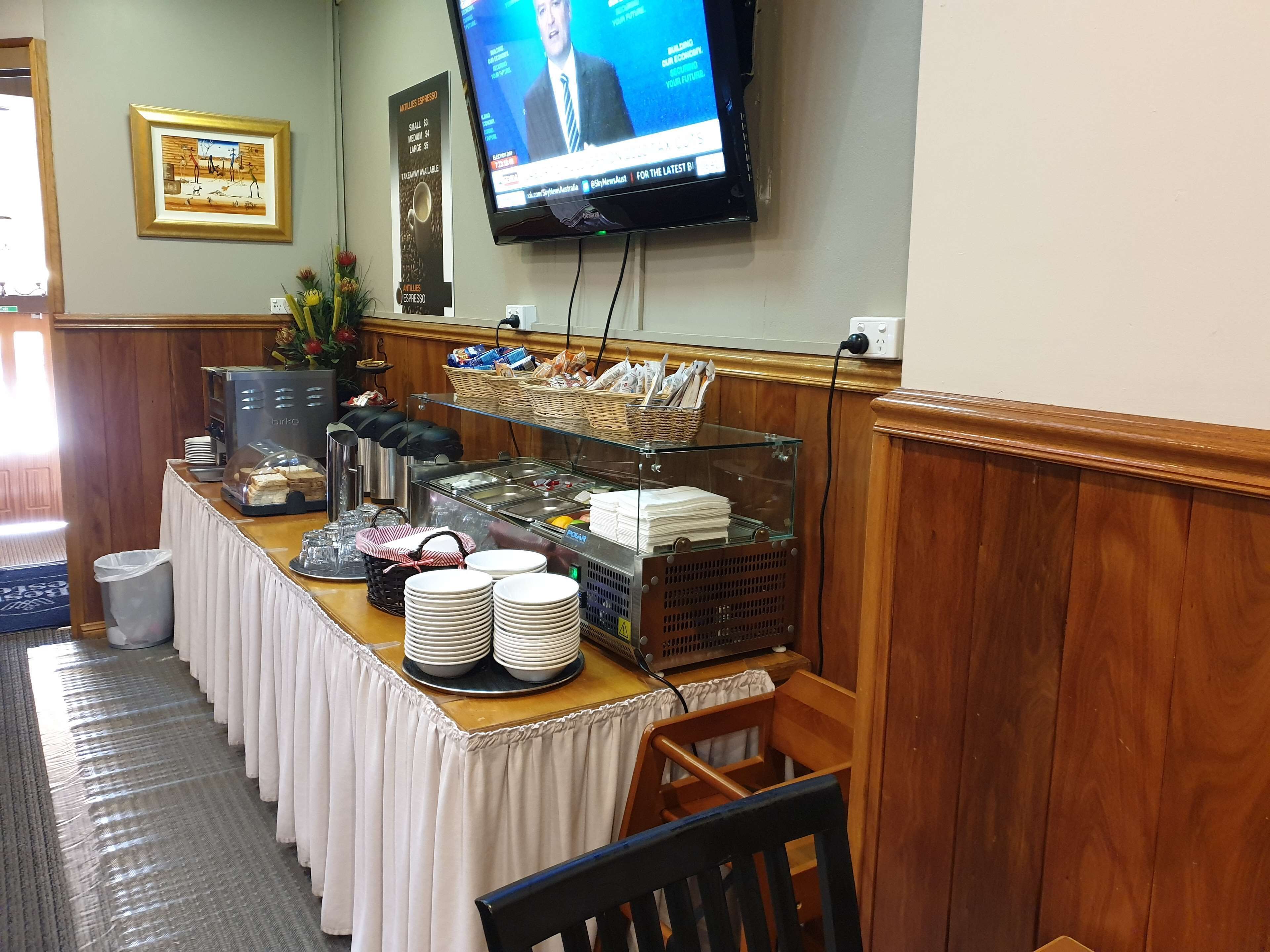 A buffet setup with a coffee machine, various food items, and a television displaying a news channel.