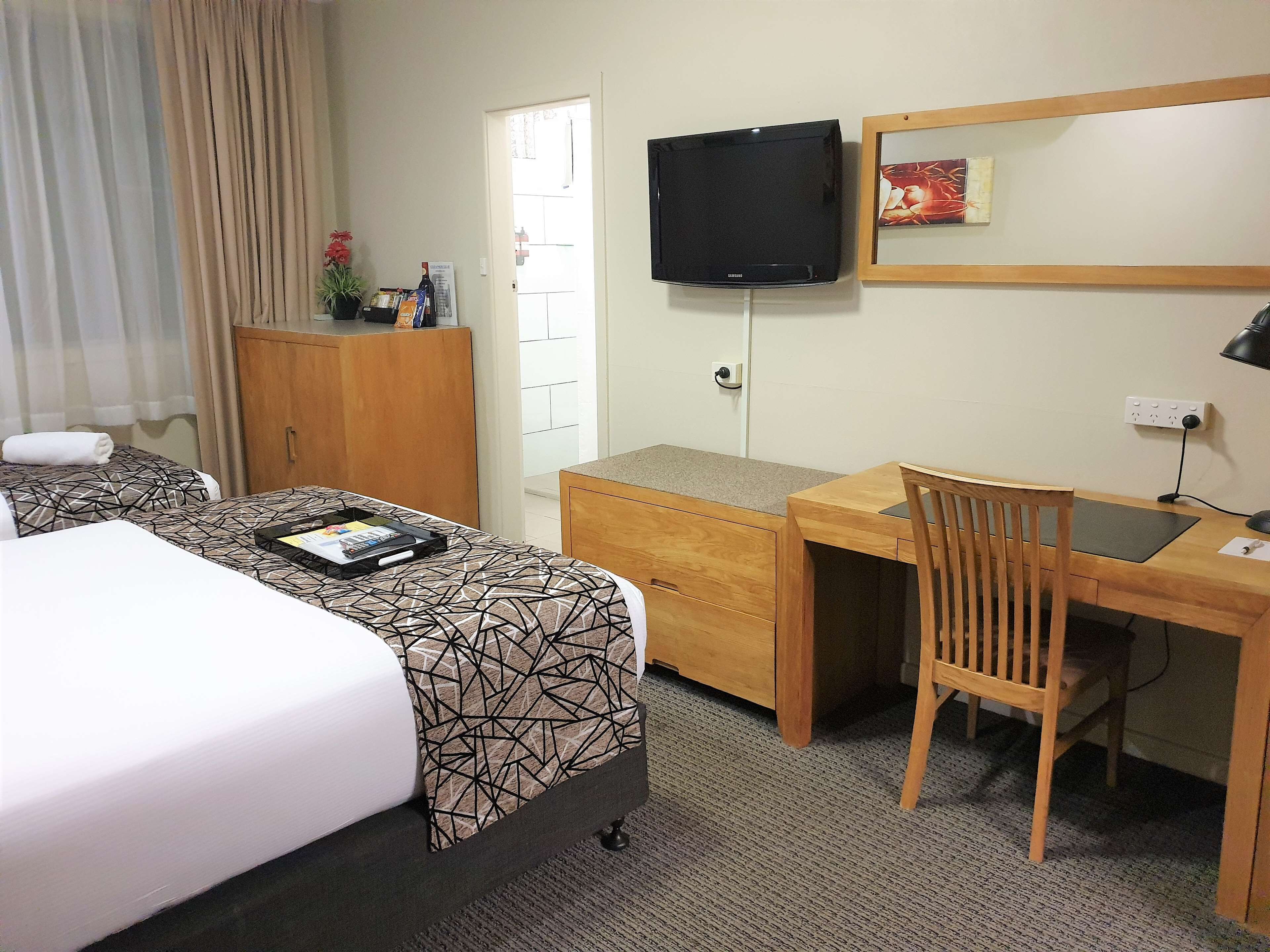 A hotel room with a bed, a desk, a chair, a television, and a wardrobe.
