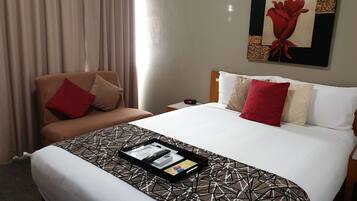 A hotel room with a bed, a chair, a nightstand, and a painting on the wall.