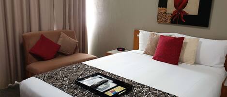 A hotel room with a bed, a chair, a nightstand, and a painting on the wall.