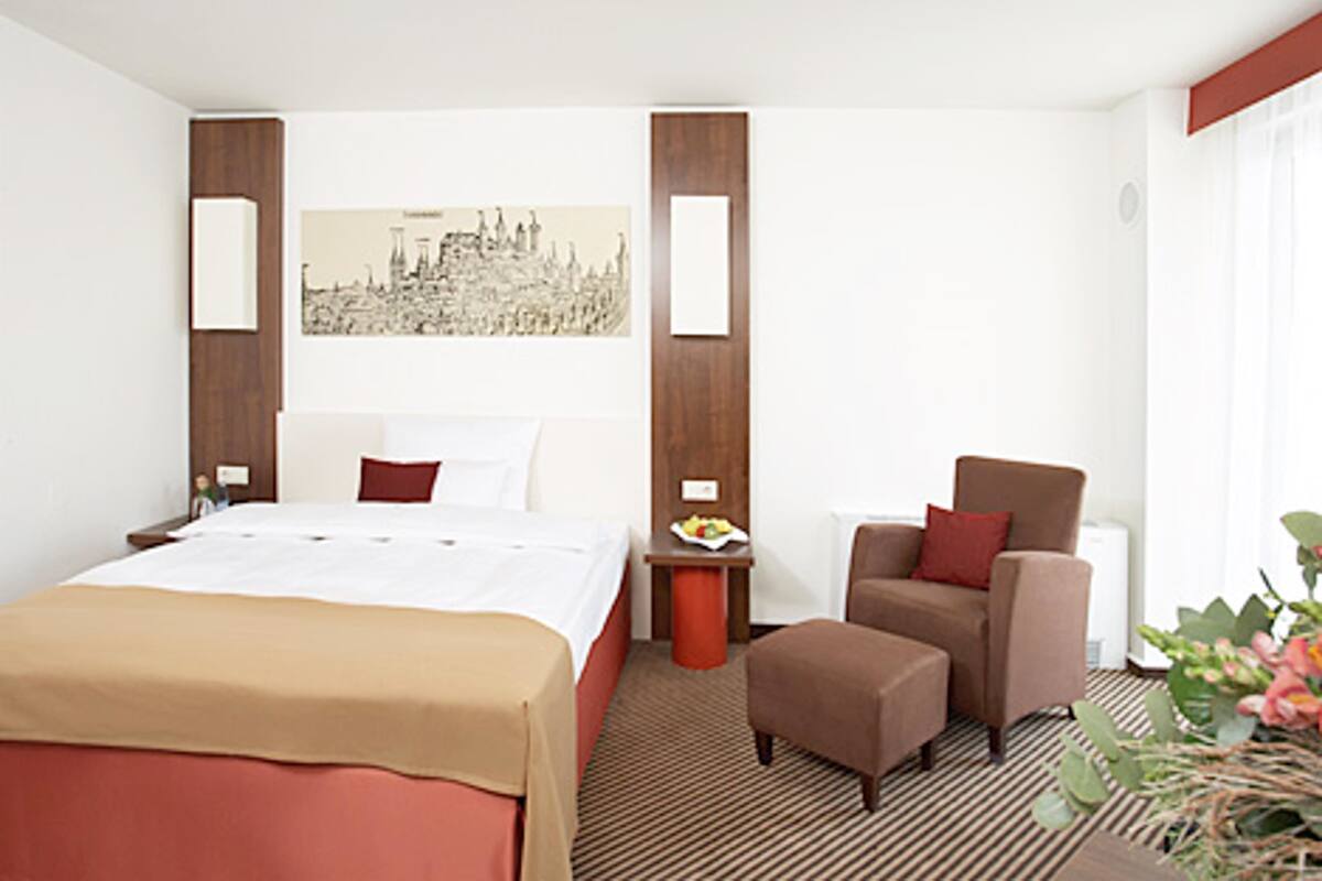A hotel room with a bed, a chair, a small table, and a wall-mounted artwork.