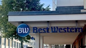 En hotellentrén med en skylt som visar ”Best Western”, utomhusservering och en parkeringsplats.