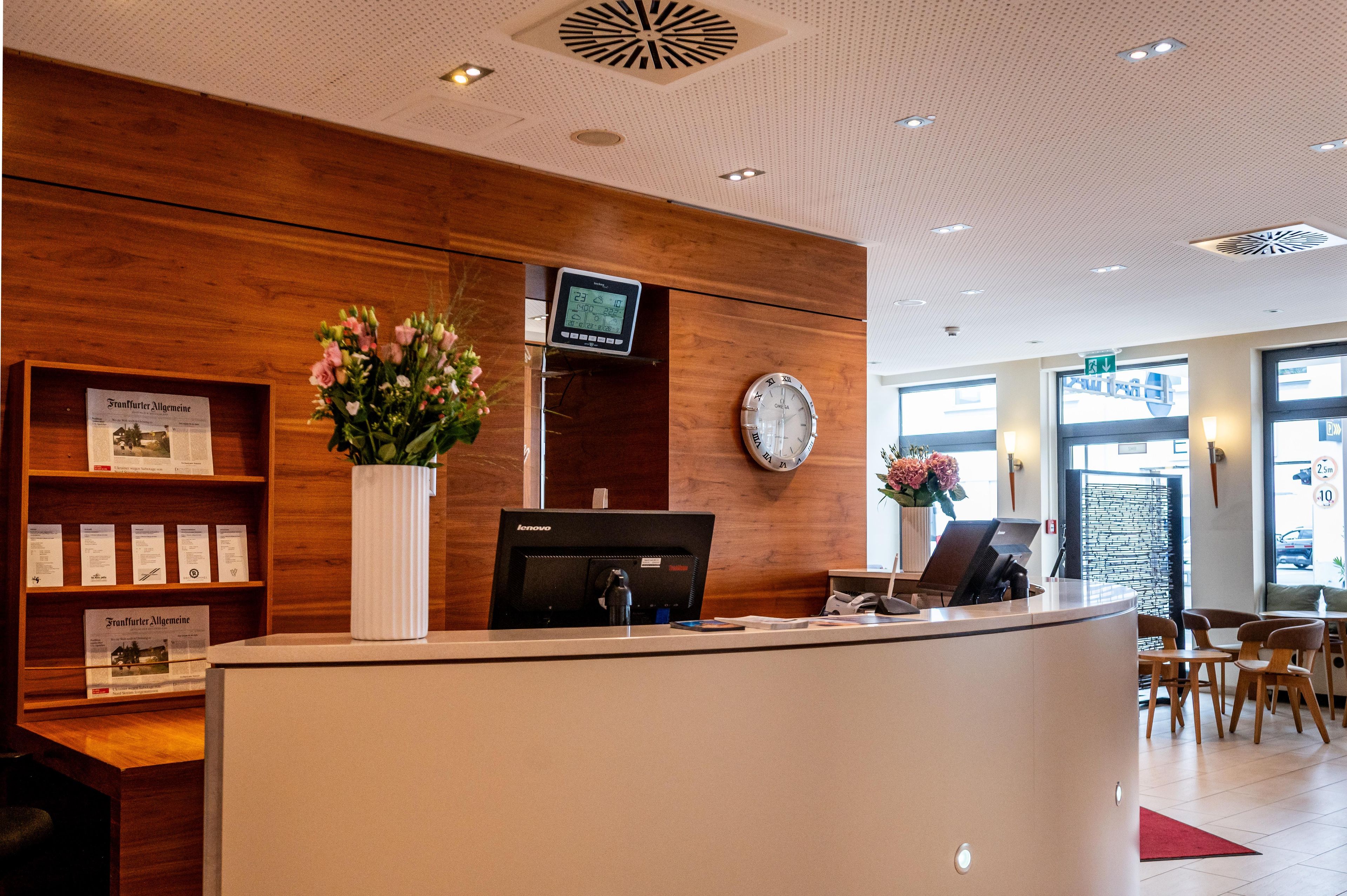 A reception desk with a digital clock, a wall clock, and informational brochures.