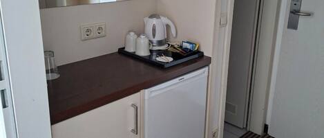 A compact kitchenette with a microwave, kettle, and coffee maker on the counter, a small refrigerator below, and a mirror above.