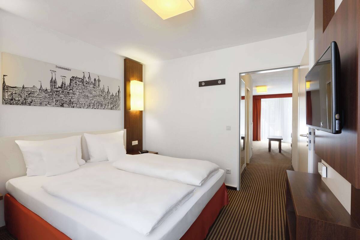 A hotel room with a large bed, a flat-screen TV, a painting of a cityscape, and a wooden accent wall.
