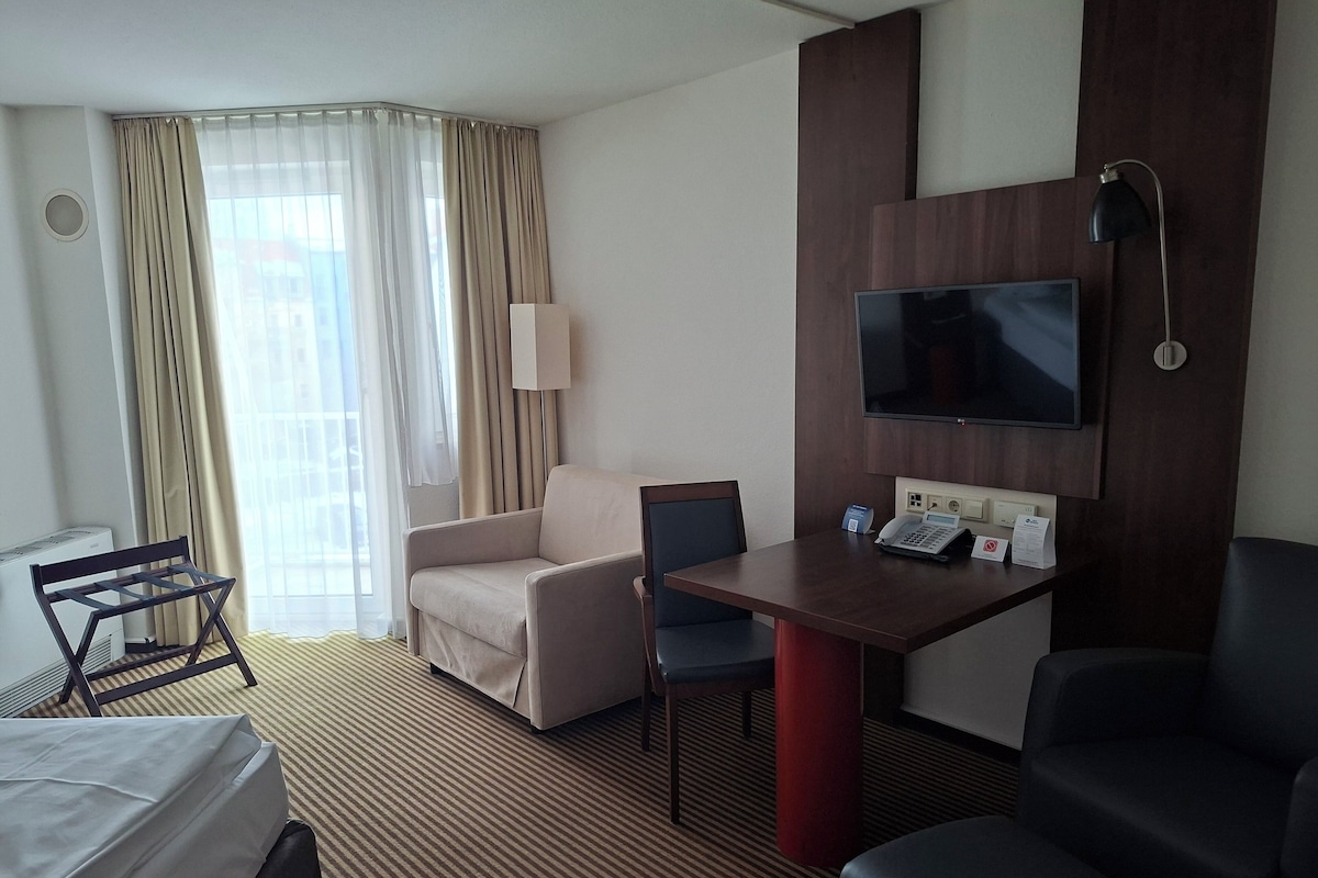 Una habitación de hotel con una cama, un escritorio con teléfono, televisión, una silla y un sofá.