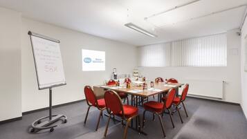 A conference room with a whiteboard, a projector screen, and a table with chairs.