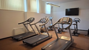 Un gimnasio con cintas de correr, bicicletas estáticas y un televisor en la pared.