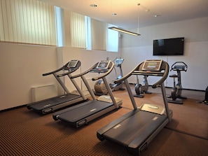 A gym with treadmills, stationary bikes, and a TV on the wall. - Best Western Hotel Nuernberg City West (Nuremberg)