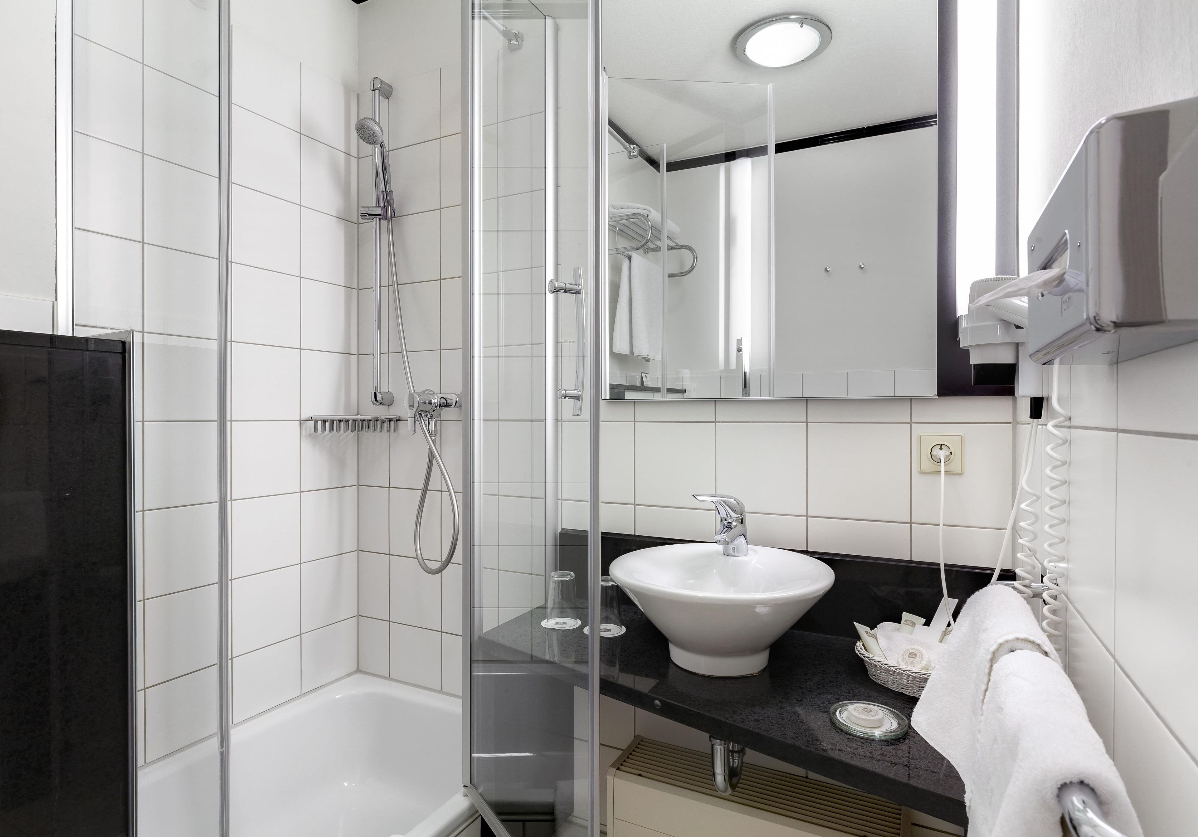 Ein modernes Badezimmer mit einer gläsernen Dusche, einem weißen Waschbecken und einer schwarzen Arbeitsplatte.