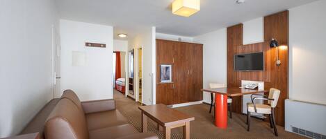 A hotel room with a sofa, a dining table, a TV, and a small kitchen area.