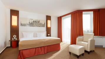 A hotel room with a bed, a chair, a cityscape artwork, and a window with curtains.