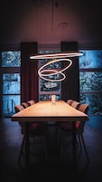 Un comedor moderno con una larga mesa de madera, seis sillas con estampado y una lámpara circular original.