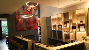 A modern bar area with a counter, stools, and a large abstract painting. - CVJM Düsseldorf Hotel & Tagung (Düsseldorf)