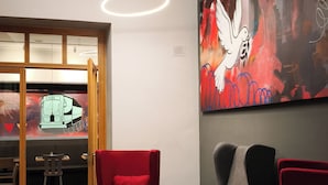 A modern waiting area with a red and black color scheme, featuring a reception desk, two red chairs, and a grey sofa. - CVJM Düsseldorf Hotel & Tagung (Düsseldorf)