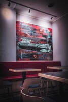 Un ristorante con un'ampia pittura astratta appesa al muro, tavoli e sedie in legno e posti a sedere imbottiti di rosso.