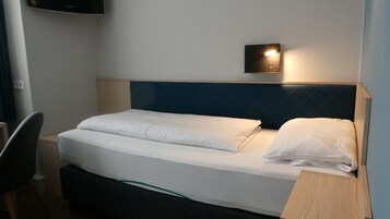Una cama bien tendida con sábanas blancas, un cabecero oscuro y una lámpara de pared.