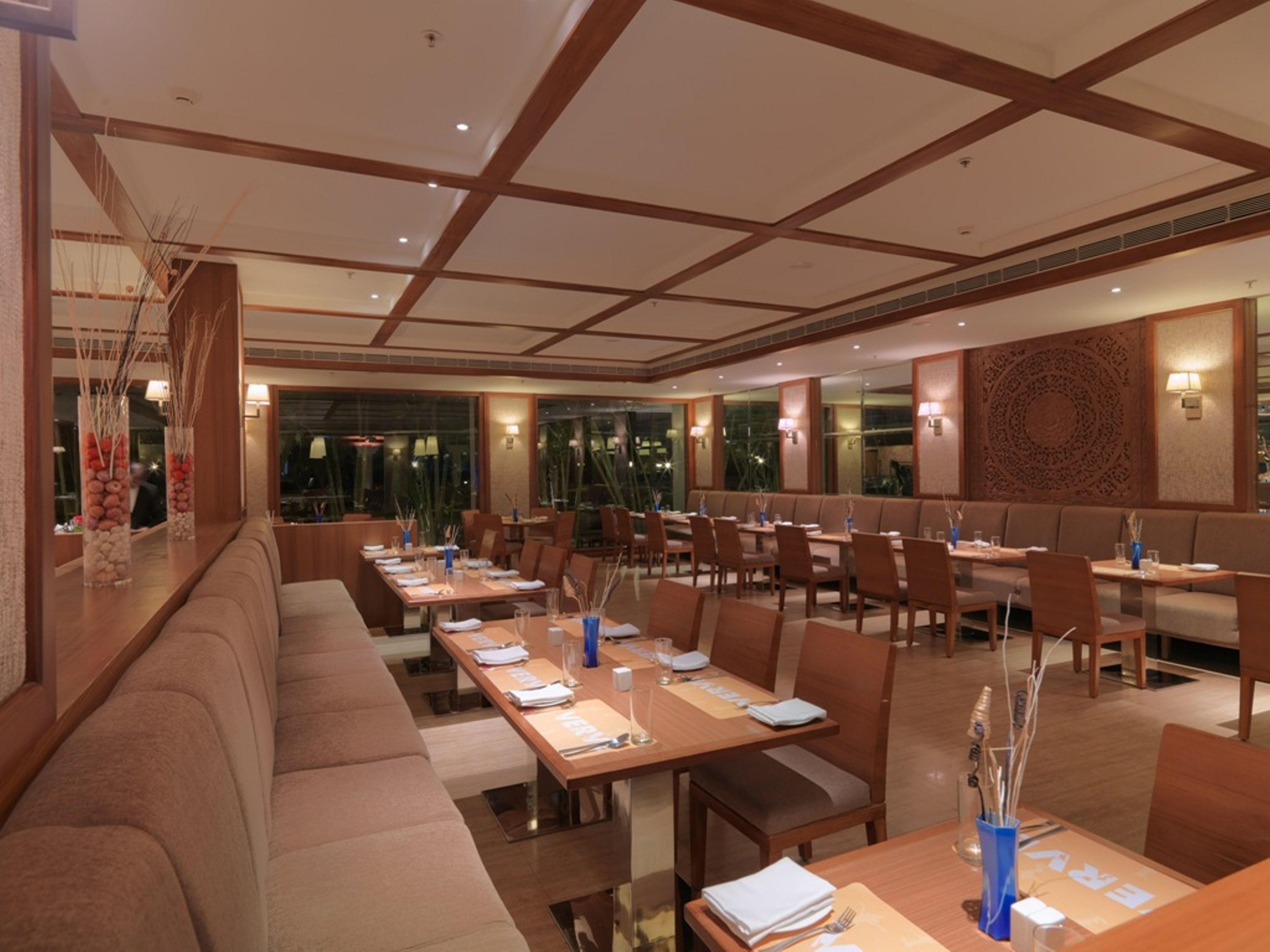 Ein geräumiges Restaurant mit langen Tischen und Sitzgelegenheiten, moderner Beleuchtung und Blick auf die Stadt durch große Fenster.