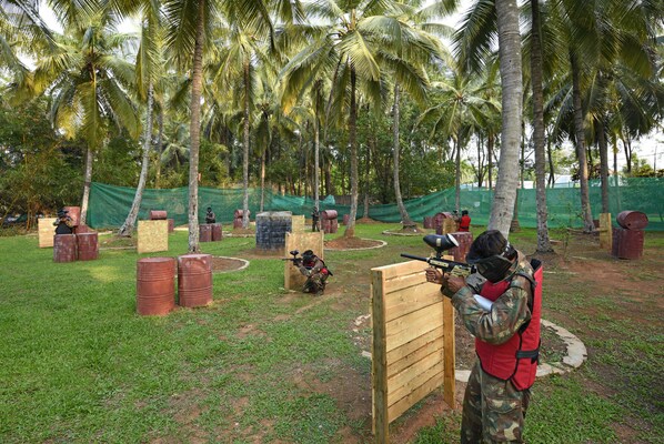 A paintball field with wooden barriers, barrels, and palm trees. - Royal Orchid Resort & Convention Centre (Bengaluru)